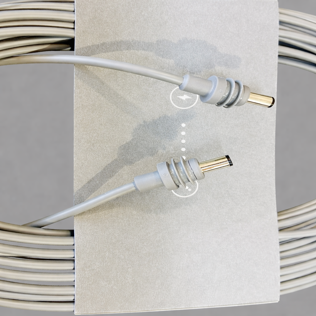 Close-up view of the Original Starlink 15-meter DC cable connectors for Starlink Mini, highlighting the metal-tipped barrel plugs and grey cardboard sleeve, with subtle product shadows on a soft grey surface