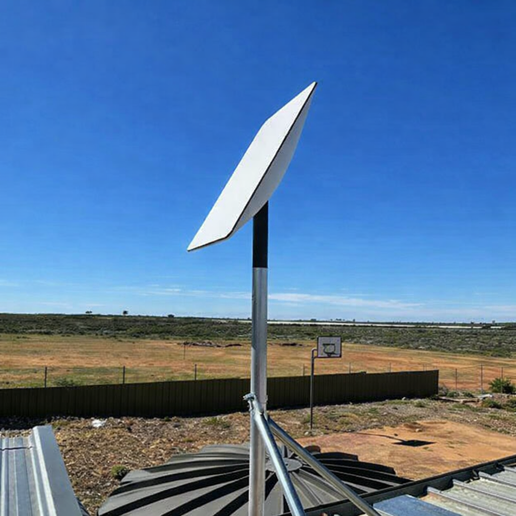 Starlink satellite dish mounted on a metal pole on a rooftop, angled toward the sky in a rural outdoor setting